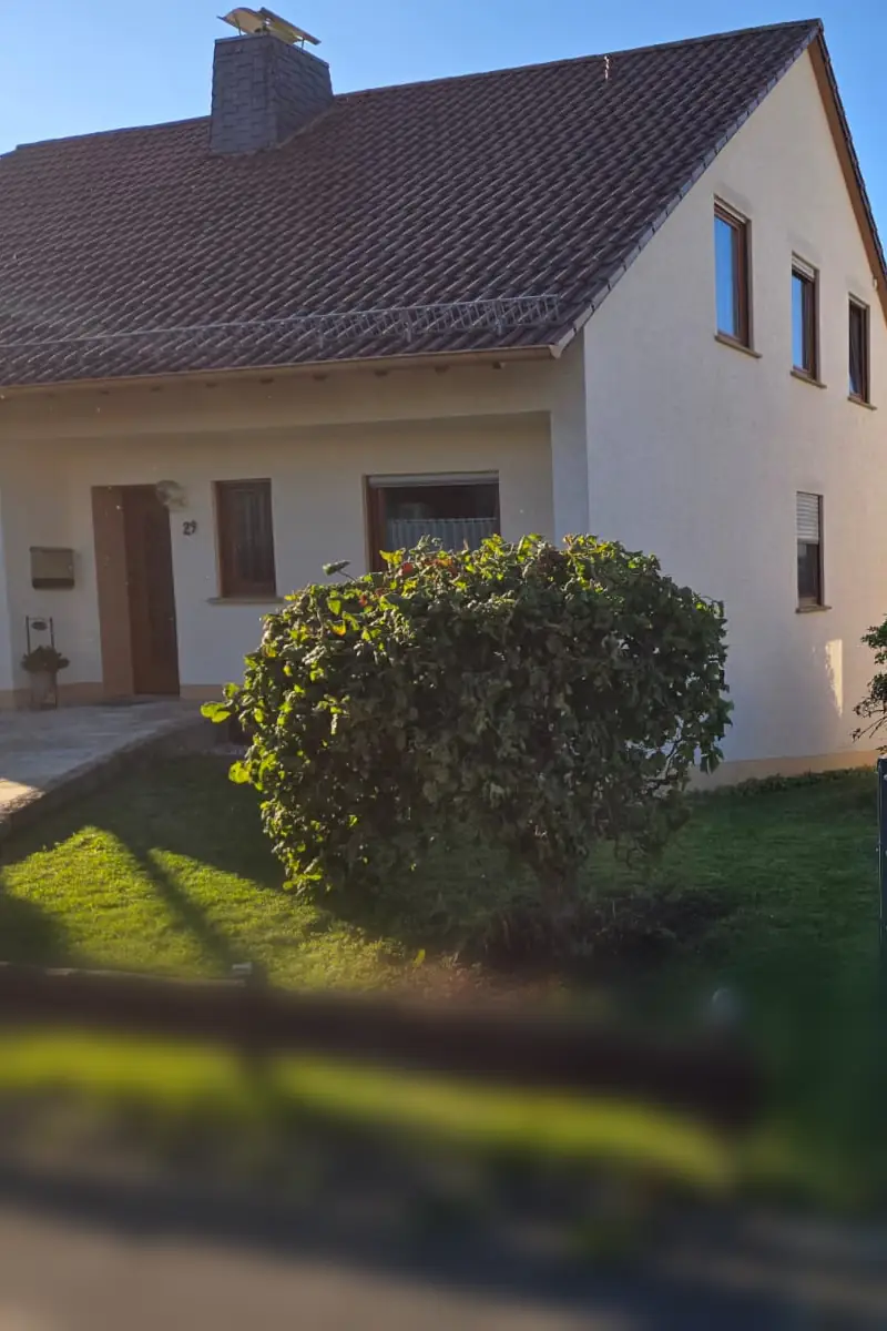 Weißes Einfamilienhaus mit gepflegtem Vorgarten und rund geschnittenem Strauch
