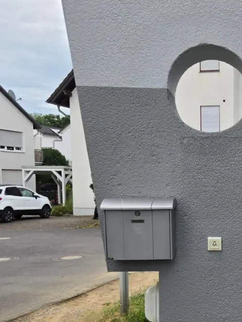 Frisch gestrichene, graue Fassade mit rundem Wanddurchbruch und Briefkasten