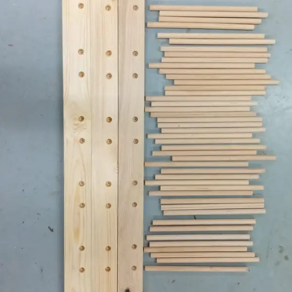 Gebohrtes Brett aus hellem Holz neben einem Stapel Rundstäbe