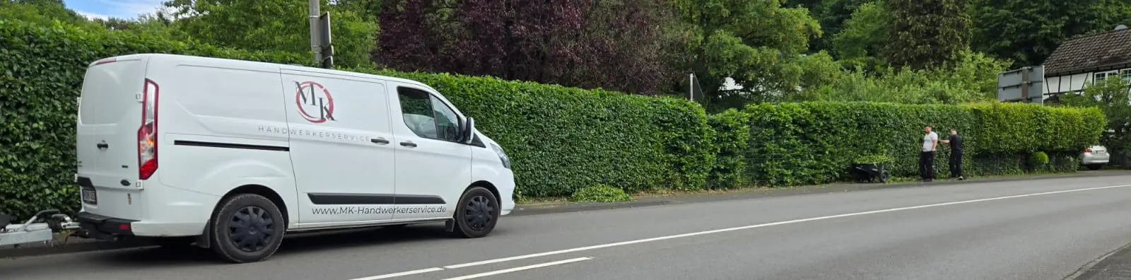 Transporter von MK-Handwerkerservice mit Logo vor einer frisch geschnittenen Buchenhecke, im Hintergrund wird weiter geschnitten