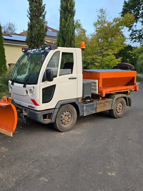 Weißes Räumfahrzeug mit Räumschild vorne und orangefarbenem Streuer auf der Ladefläche