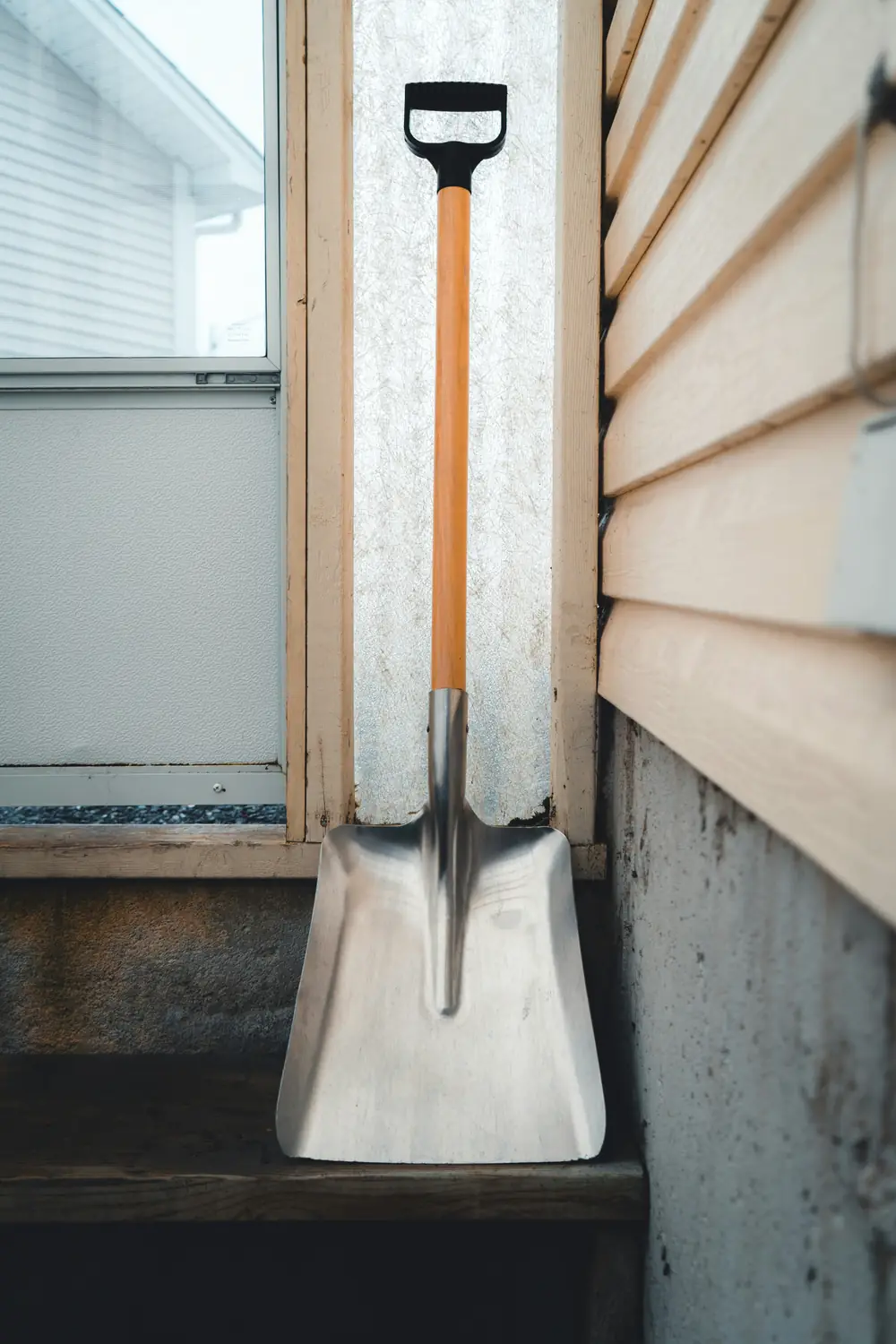 Schneeschaufel lehnt an einer Hauswand neben der Tür